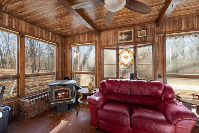 sunroom featuring beamed ceiling, ceiling fan, a wood stove, and wood ceiling