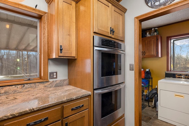 kitchen featuring stainless steel double oven, washer / dryer, and light stone countertops