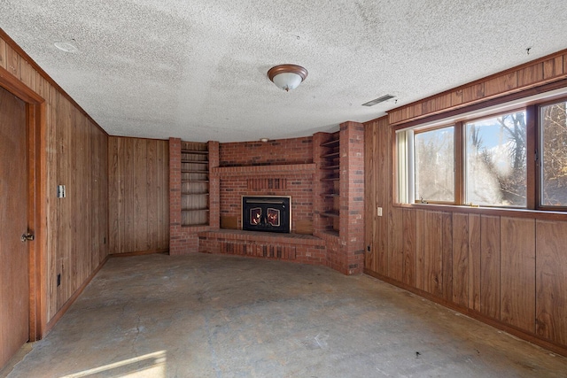 unfurnished living room featuring a fireplace, a textured ceiling, and wood walls