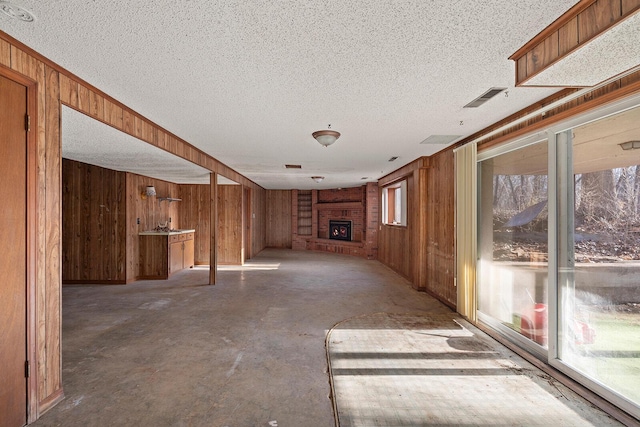 unfurnished living room featuring a fireplace, concrete flooring, a textured ceiling, and wood walls