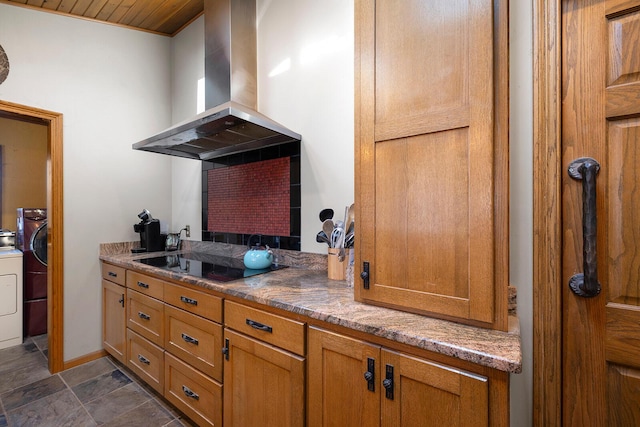 kitchen featuring black electric cooktop, island range hood, washing machine and clothes dryer, and stone countertops