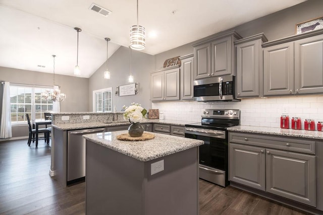 kitchen featuring stainless steel appliances, light stone countertops, a center island, and decorative light fixtures