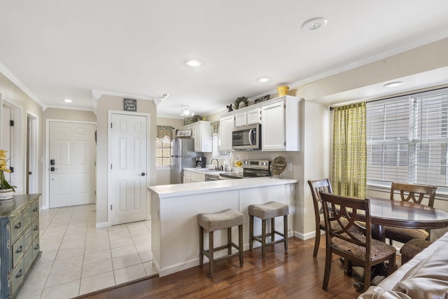 kitchen featuring light tile patterned flooring, white cabinets, kitchen peninsula, stainless steel appliances, and crown molding