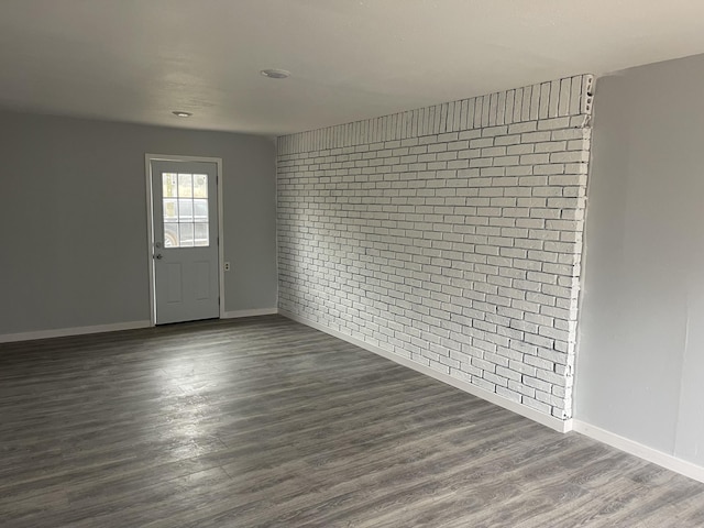 spare room with dark hardwood / wood-style flooring and brick wall