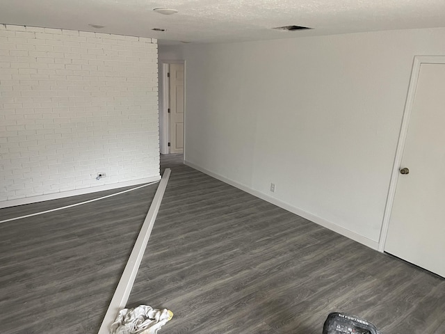 empty room featuring brick wall, dark hardwood / wood-style flooring, and a textured ceiling