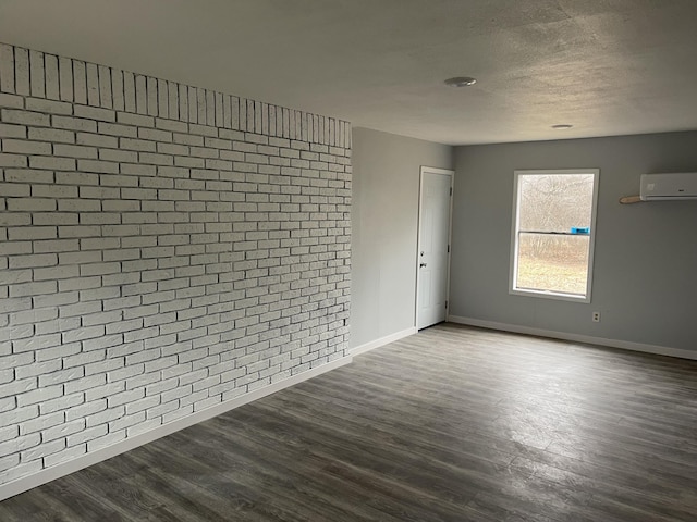 empty room featuring brick wall, a wall mounted air conditioner, wood-type flooring, and a textured ceiling