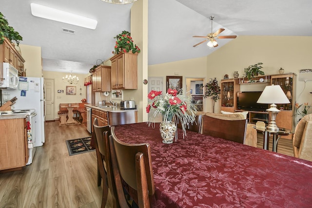 dining area with vaulted ceiling, sink, ceiling fan with notable chandelier, and light wood-type flooring