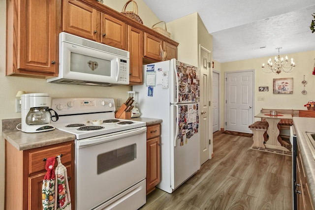 kitchen featuring an inviting chandelier, hanging light fixtures, white appliances, a textured ceiling, and light wood-type flooring