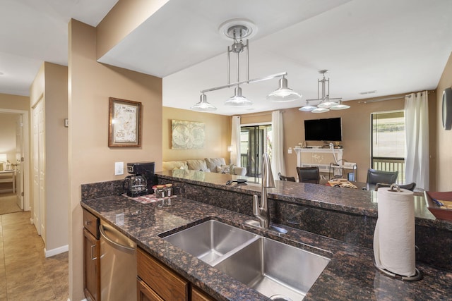 kitchen with hanging light fixtures, stainless steel dishwasher, sink, and dark stone counters