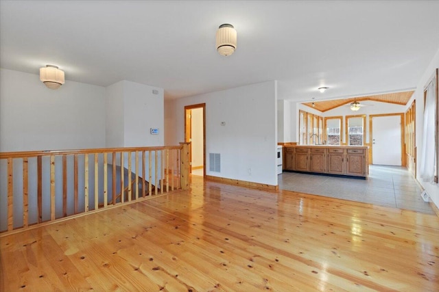 empty room featuring sink, vaulted ceiling, and light wood-type flooring