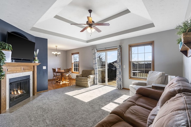 living room with a tiled fireplace, ceiling fan with notable chandelier, and a raised ceiling