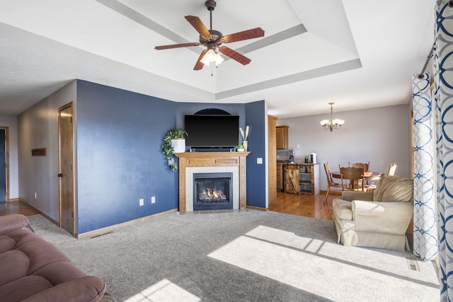 living room featuring a tray ceiling, ceiling fan with notable chandelier, and a tile fireplace