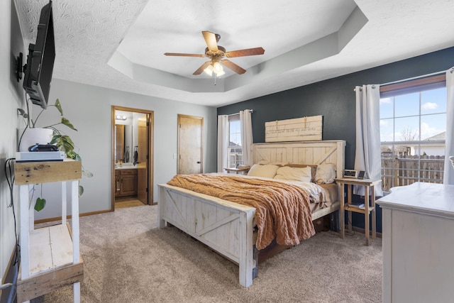 bedroom with ensuite bathroom, ceiling fan, a tray ceiling, light carpet, and a textured ceiling