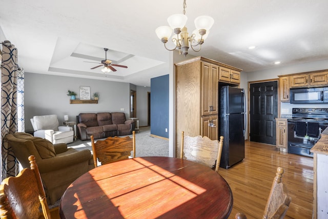 dining space with dark hardwood / wood-style flooring, a raised ceiling, and ceiling fan with notable chandelier