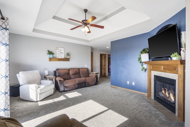 living room with ceiling fan, a raised ceiling, carpet floors, and a tile fireplace