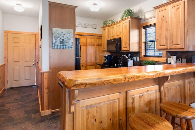 kitchen featuring tasteful backsplash, a kitchen bar, butcher block countertops, and black appliances