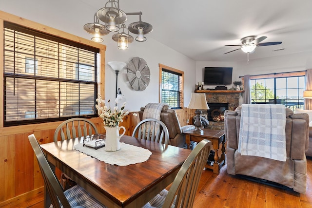 dining area with wood-type flooring, ceiling fan, a fireplace, and wood walls