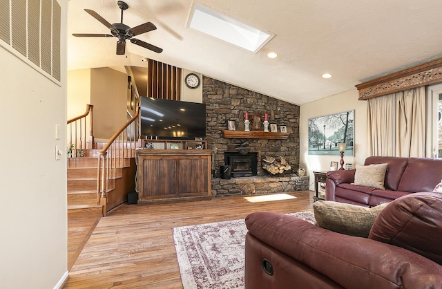 living room featuring ceiling fan, light hardwood / wood-style flooring, and vaulted ceiling with skylight