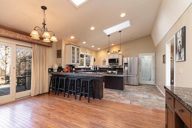 kitchen with light hardwood / wood-style flooring, appliances with stainless steel finishes, a kitchen breakfast bar, vaulted ceiling with skylight, and decorative light fixtures