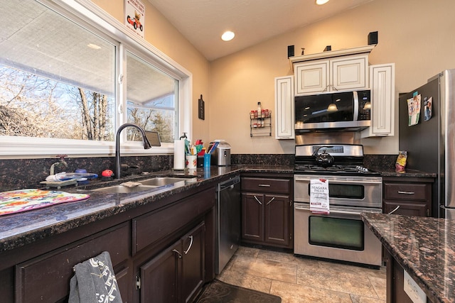 kitchen with lofted ceiling, sink, appliances with stainless steel finishes, dark stone countertops, and dark brown cabinetry