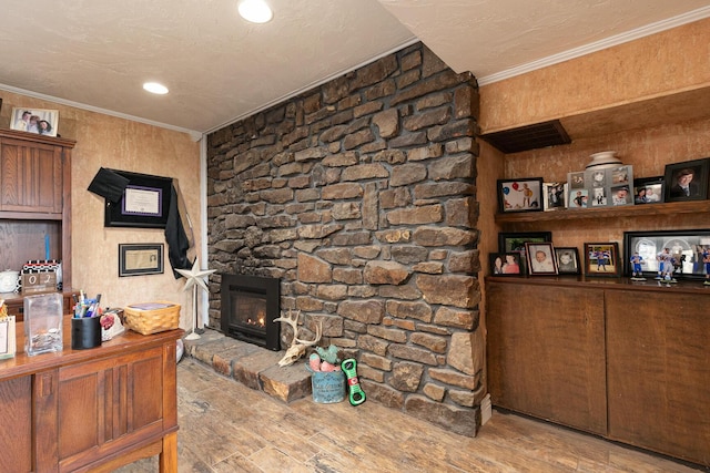 living room featuring crown molding, a stone fireplace, a textured ceiling, and light hardwood / wood-style floors