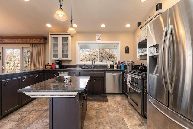 kitchen featuring appliances with stainless steel finishes, decorative light fixtures, dark stone countertops, a center island, and a healthy amount of sunlight