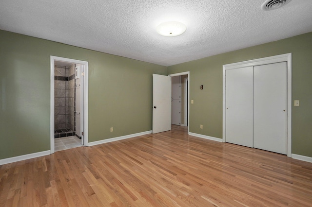 unfurnished bedroom featuring ensuite bath, a closet, a textured ceiling, and light wood-type flooring