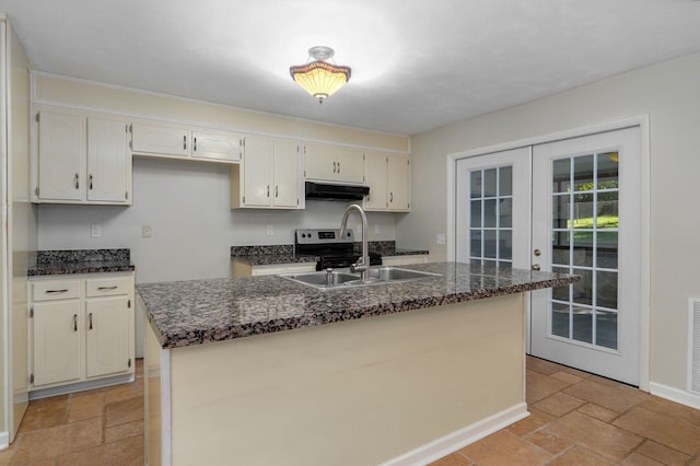 kitchen featuring french doors, a kitchen island with sink, sink, and dark stone countertops