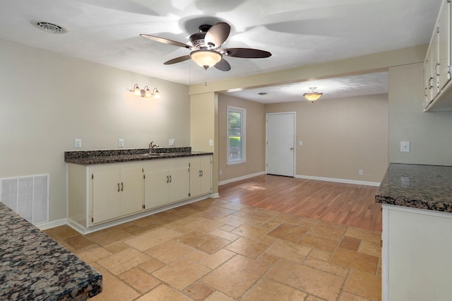 kitchen with sink, white cabinets, ceiling fan, and dark stone counters