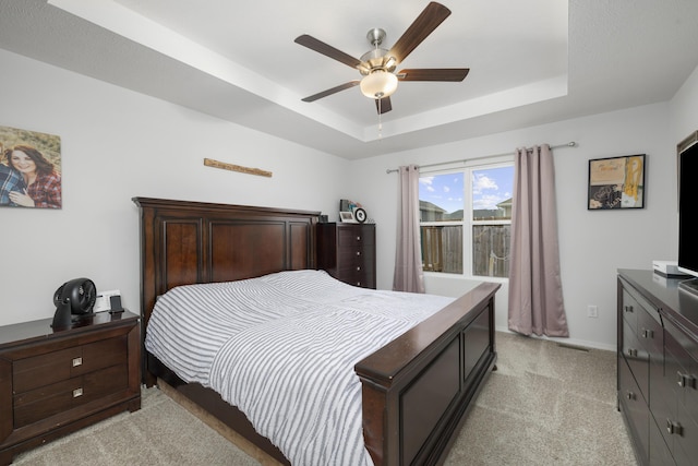 carpeted bedroom featuring ceiling fan and a tray ceiling