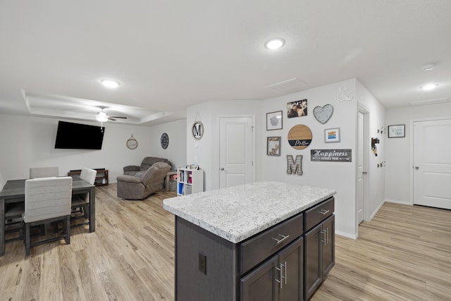 kitchen with light hardwood / wood-style flooring, ceiling fan, a center island, dark brown cabinetry, and a tray ceiling