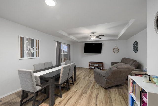 dining room with a raised ceiling, ceiling fan, and light wood-type flooring