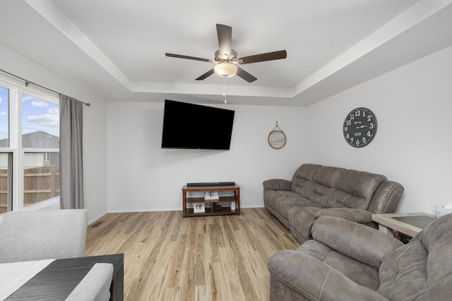 living room with ceiling fan, a tray ceiling, and light hardwood / wood-style floors