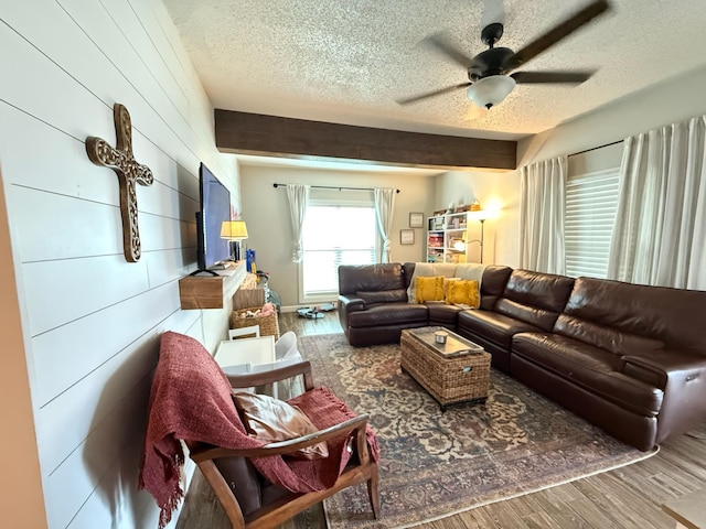 living room with ceiling fan, hardwood / wood-style flooring, beamed ceiling, and a textured ceiling