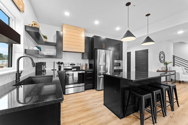 kitchen with sink, dark stone countertops, hanging light fixtures, stainless steel appliances, and a kitchen breakfast bar