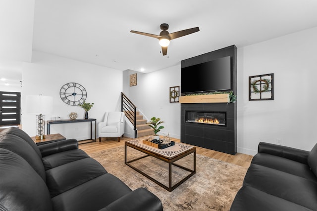 living room featuring ceiling fan, a large fireplace, and light wood-type flooring