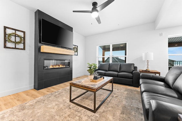 living room featuring ceiling fan, wood-type flooring, a large fireplace, and a healthy amount of sunlight