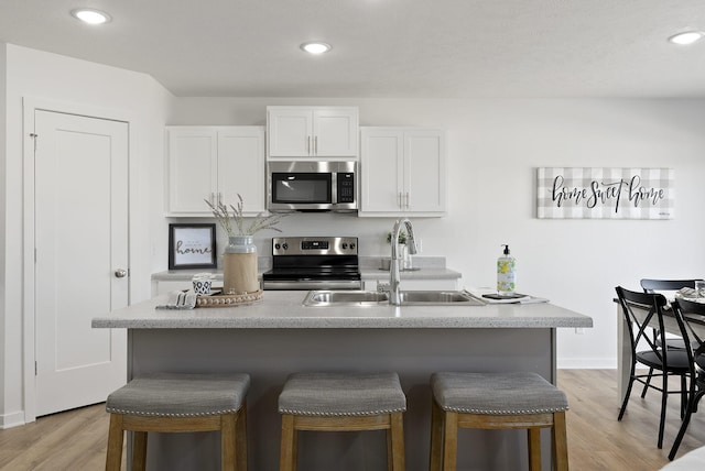 kitchen with sink, white cabinets, light hardwood / wood-style floors, stainless steel appliances, and a center island with sink