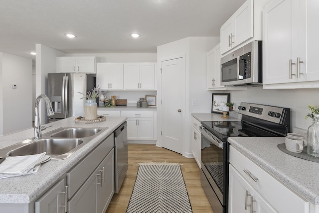 kitchen featuring sink, a center island with sink, appliances with stainless steel finishes, light hardwood / wood-style floors, and white cabinets