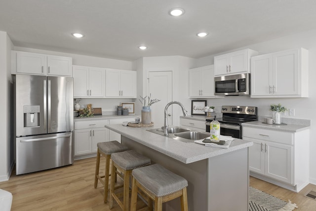 kitchen featuring stainless steel appliances, a kitchen breakfast bar, light hardwood / wood-style floors, white cabinets, and a center island with sink