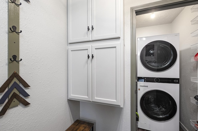 clothes washing area with stacked washer / drying machine, cabinets, and a textured ceiling