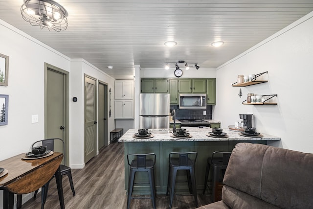 kitchen featuring light stone counters, appliances with stainless steel finishes, a kitchen breakfast bar, kitchen peninsula, and green cabinets