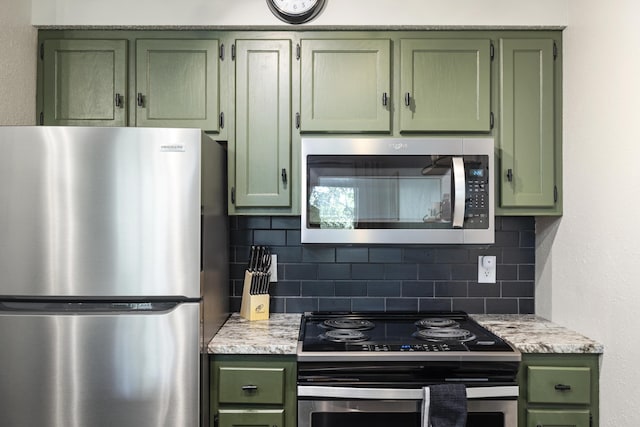 kitchen with light stone counters, backsplash, stainless steel appliances, and green cabinetry