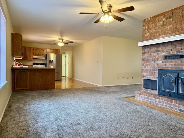 unfurnished living room featuring a brick fireplace, light colored carpet, and ceiling fan