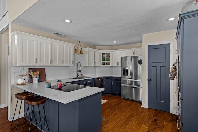 kitchen with a kitchen bar, sink, stainless steel fridge, kitchen peninsula, and white cabinets