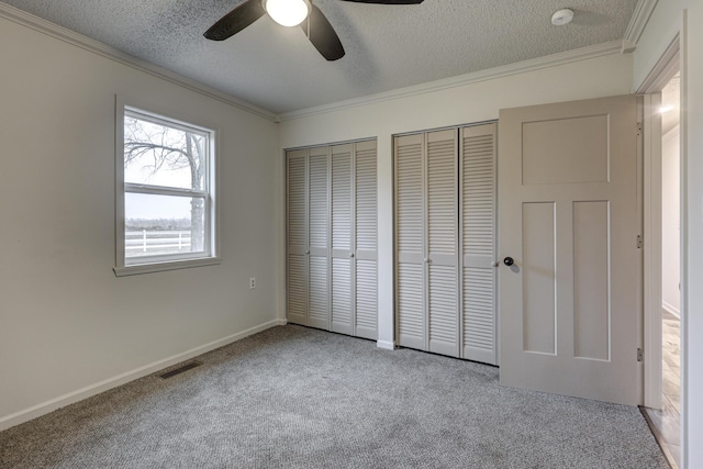 unfurnished bedroom with crown molding, a textured ceiling, multiple closets, ceiling fan, and light colored carpet