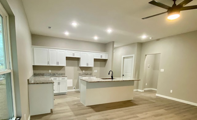 kitchen with white cabinetry, light stone countertops, a kitchen island with sink, and light hardwood / wood-style flooring