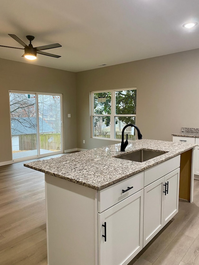 kitchen with sink, light hardwood / wood-style flooring, light stone counters, an island with sink, and white cabinets