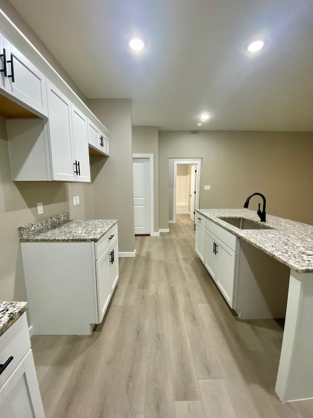 kitchen featuring white cabinetry, light stone countertops, sink, and light hardwood / wood-style floors