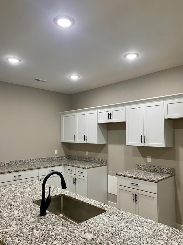 kitchen featuring white cabinetry, light stone countertops, and sink